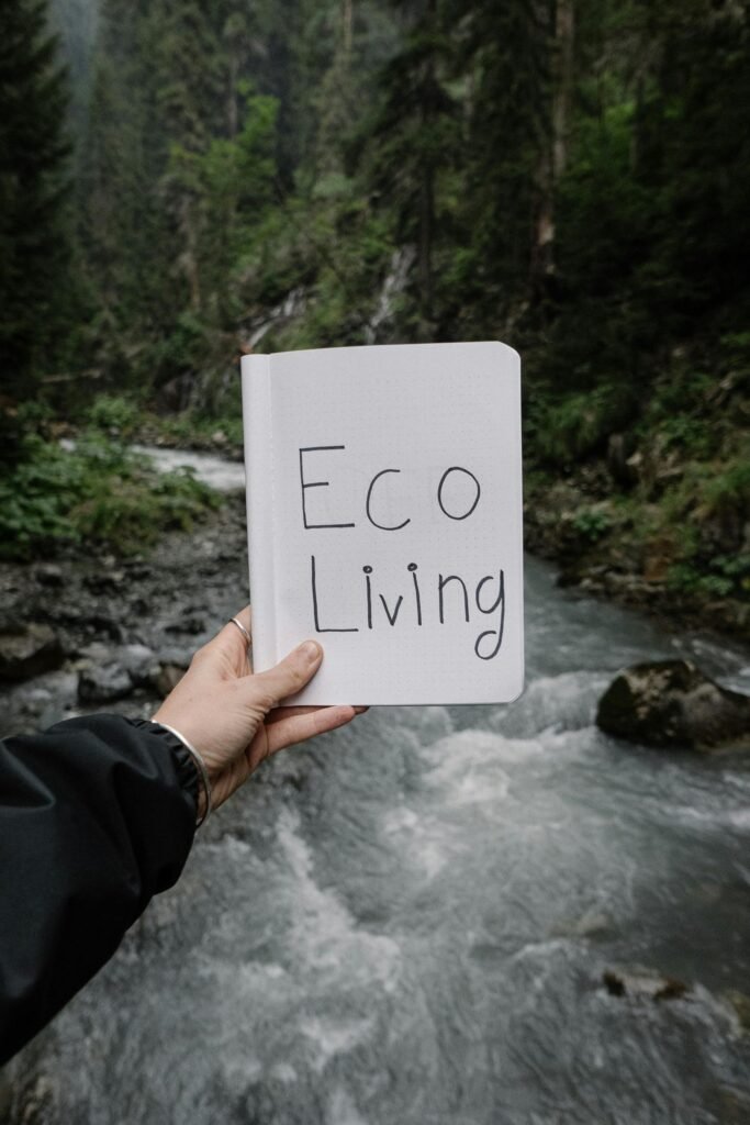 Hand holding a notebook with 'Eco Living' text against a scenic forest river backdrop.